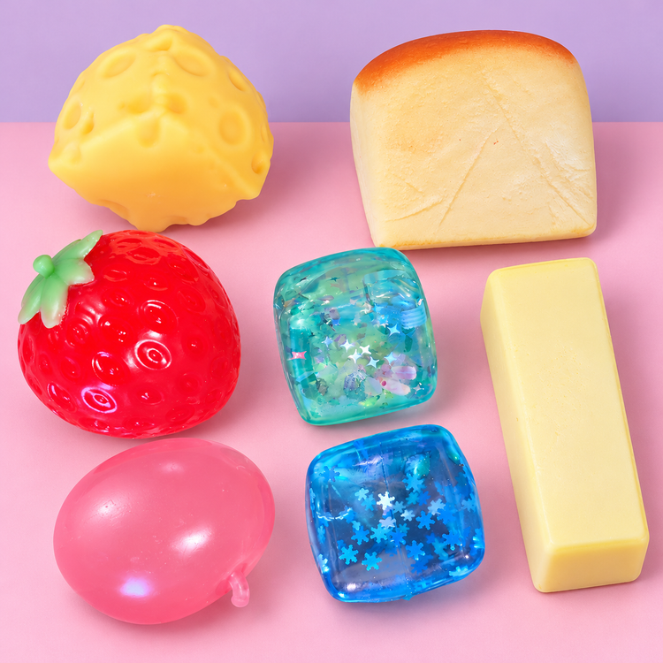 Seven of the eight squishies on a pastel pink and lilac background: cheese, toast, strawberry, teal star cube, butter stick, pink apple and blue snowflake cube